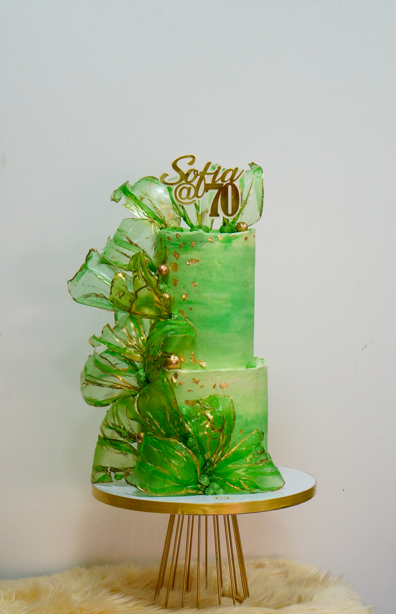 Elegant green two-tier birthday cake with gold leaf accents and large decorative green sugar sails