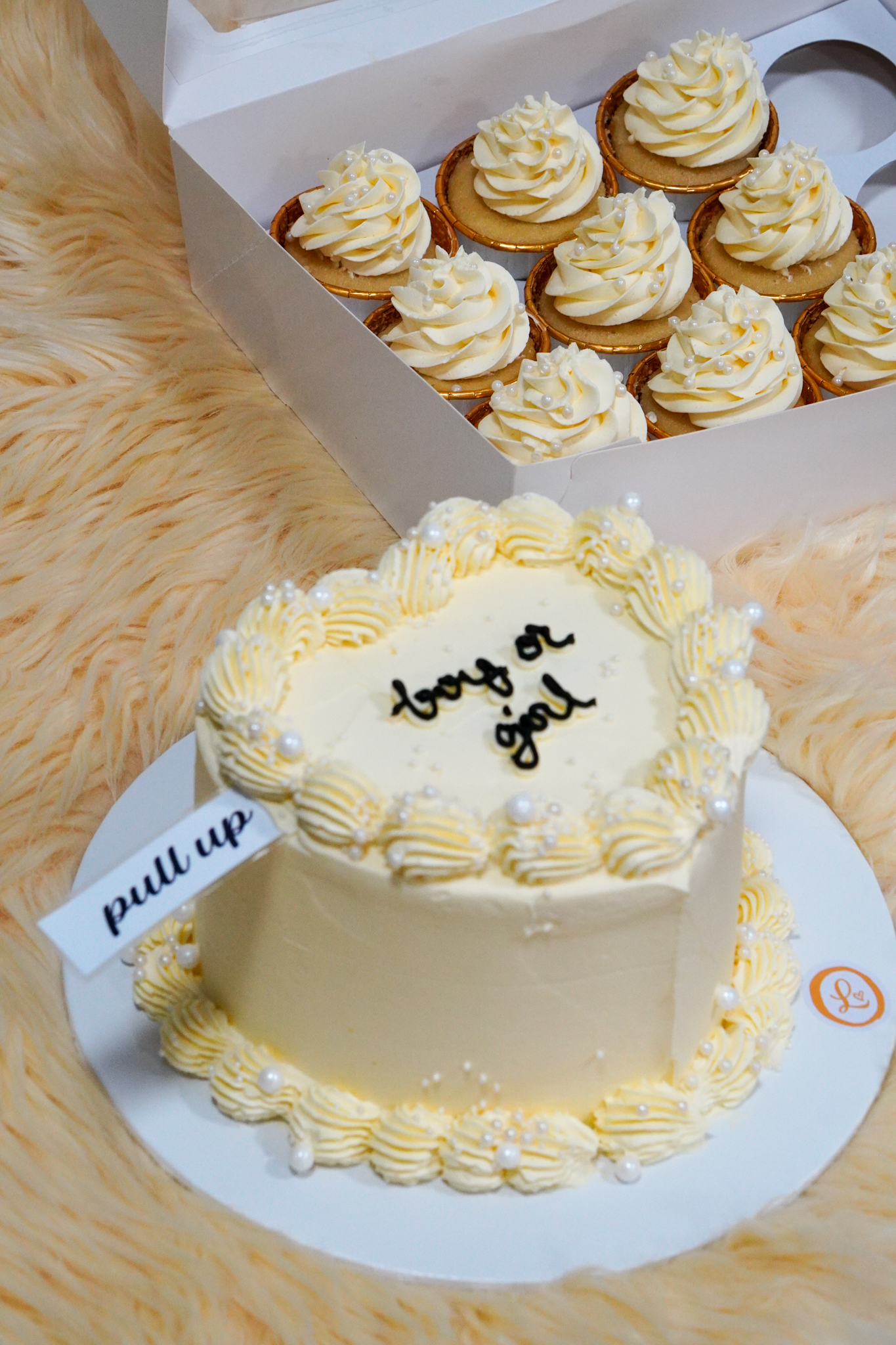 White and cream gender reveal cake with piped rosettes, pearl decorations, and matching cupcakes in a box, featuring 'boy or girl' text on top