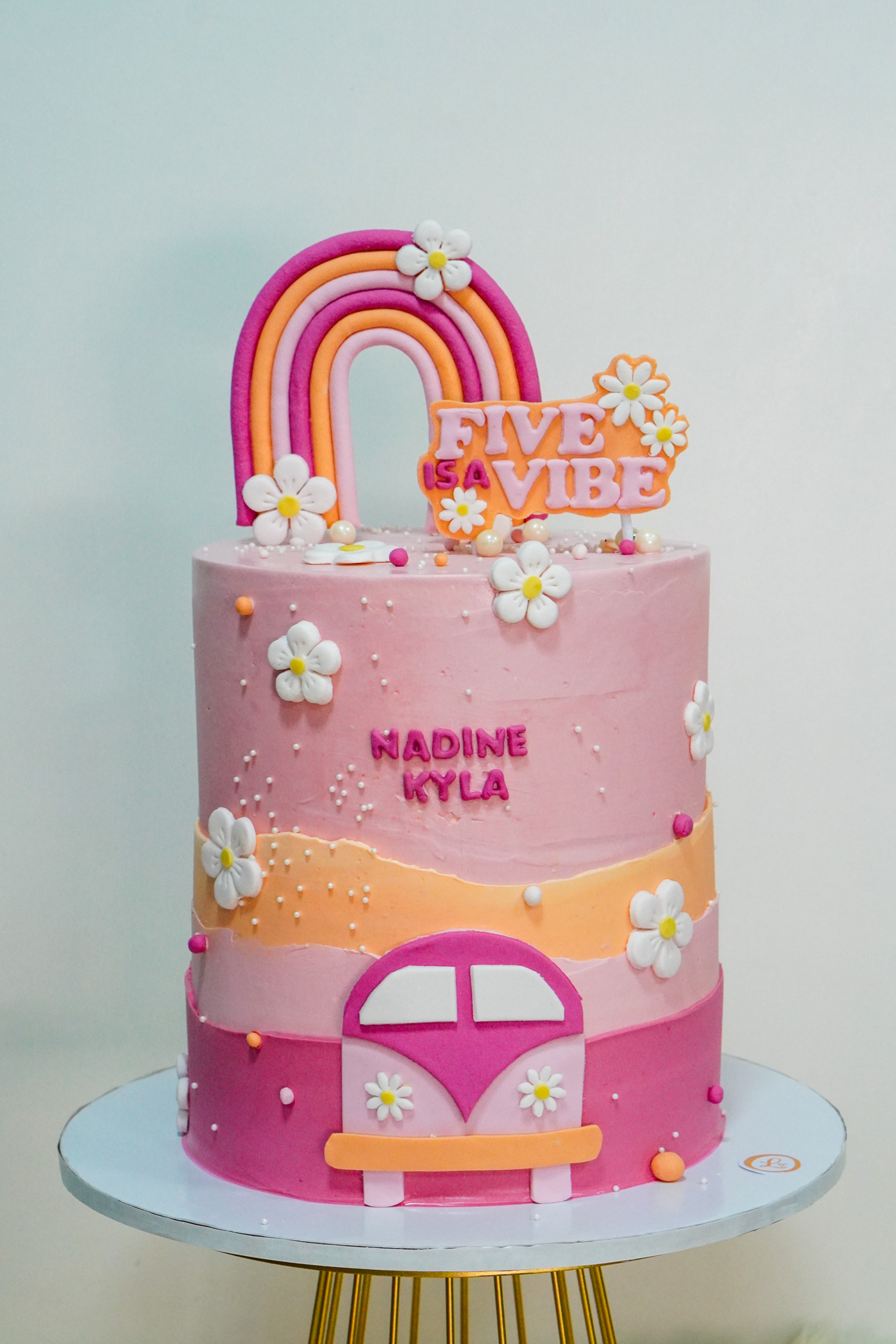 Pink and orange buttercream birthday cake with a fondant rainbow topper, white flowers, and a pink van design, featuring the text 'Five is a Vibe' and name Nadine Kyla