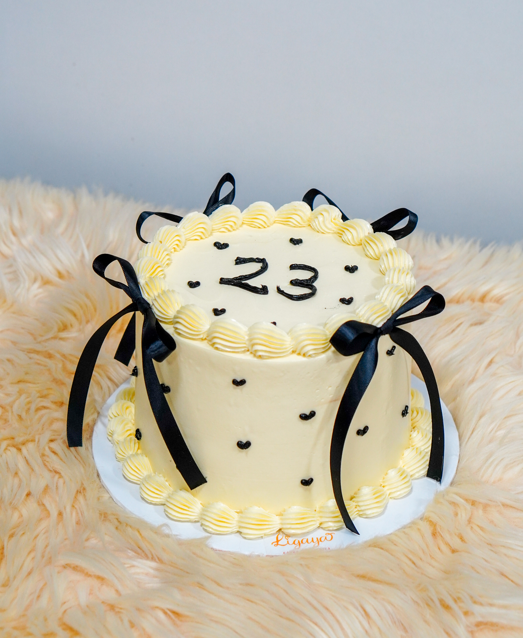 Minimalist cream birthday cake with the number 23, black heart accents, and black ribbon bows