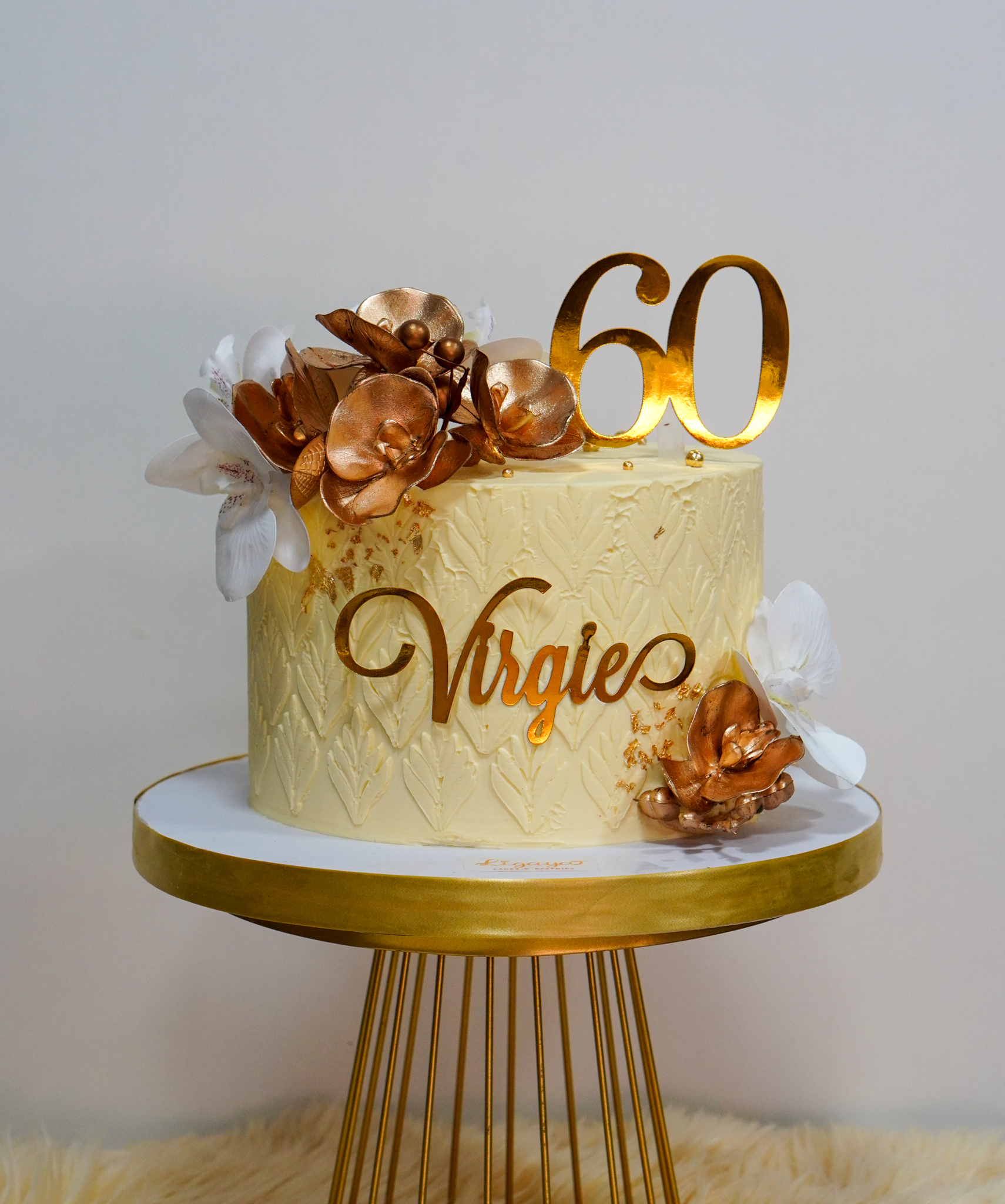 Elegant gold and cream birthday cake with metallic flowers, white orchids, and a gold number 60 topper