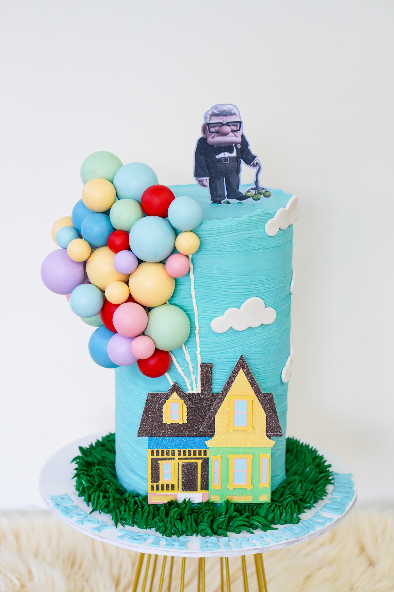 Up movie themed buttercream cake in blue with fondant house, cluster of colorful balloons, clouds, and Carl Fredricksen topper